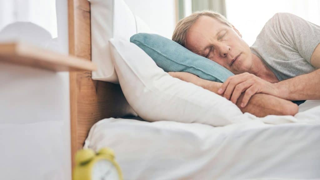 A tired, middle-aged man is sleeping in his bed during the day.