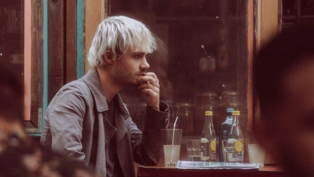 A serious man with white hair sits at a table with drinks.