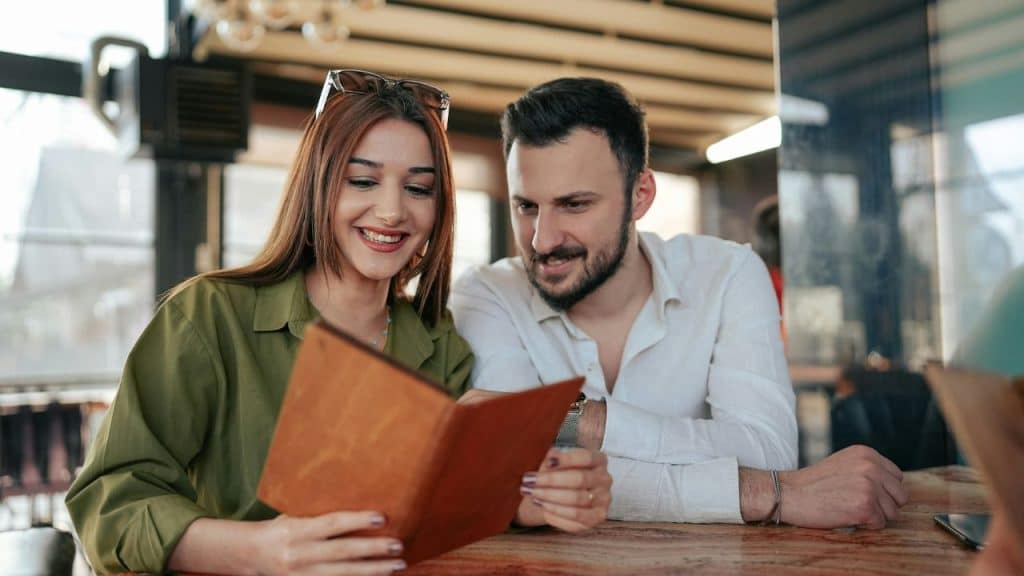 A happy couple sits together in a restaurant, looking at a menu.