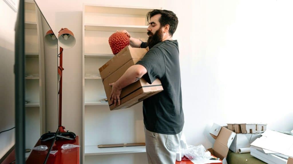A bearded man holds a large cardboard box while moving belongings into a room.