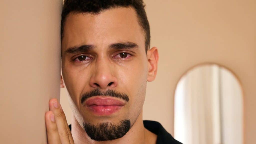 A sad man with teary eyes leans against a wall.