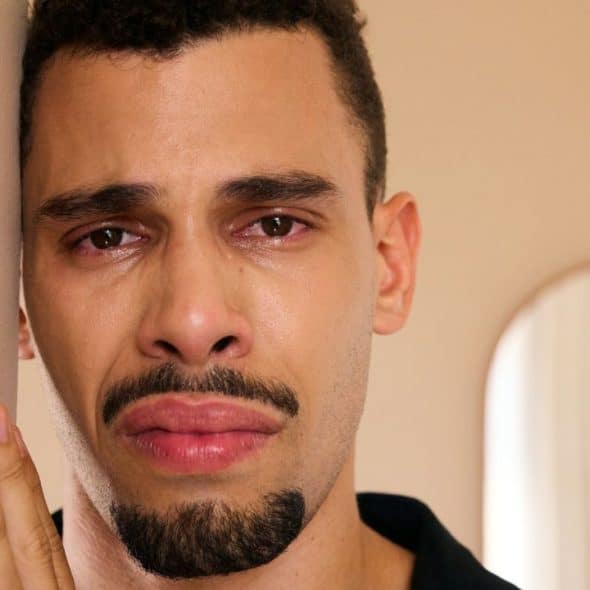 A sad man with teary eyes leans against a wall.