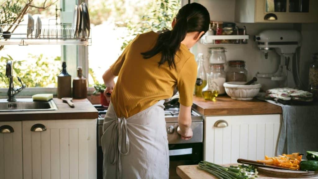 A person in an apron is cooking in a kitchen with a cutting board in the foreground.