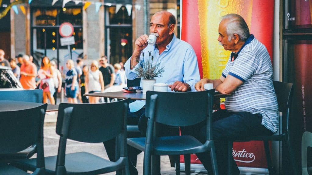 A photo shows two older men talking at an outdoor cafe.