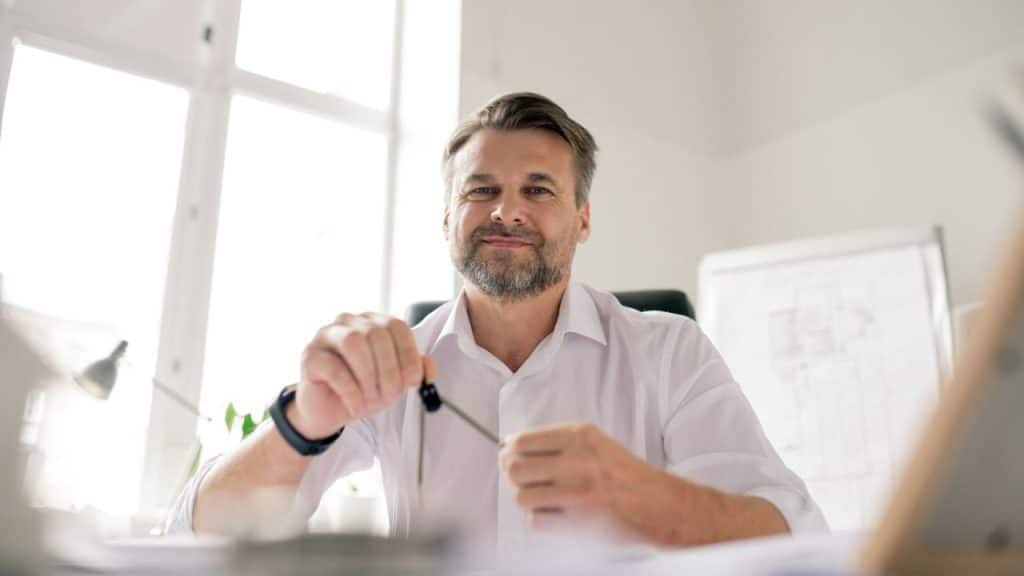 A handsome, middle-aged man with a beard holds a compass and smiles at the camera.