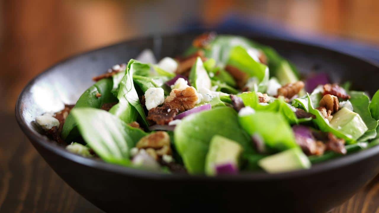 A bowl of fresh spinach salad with nuts and cheese.