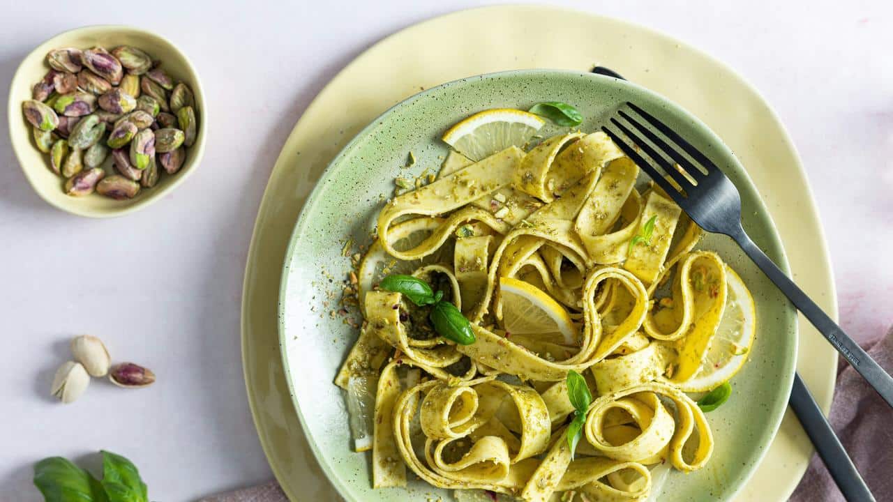 A plate of pasta with pesto and lemon slices.