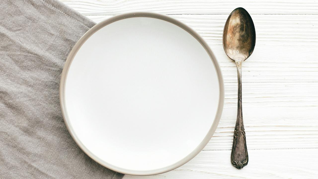 An empty white plate with a spoon placed beside it.