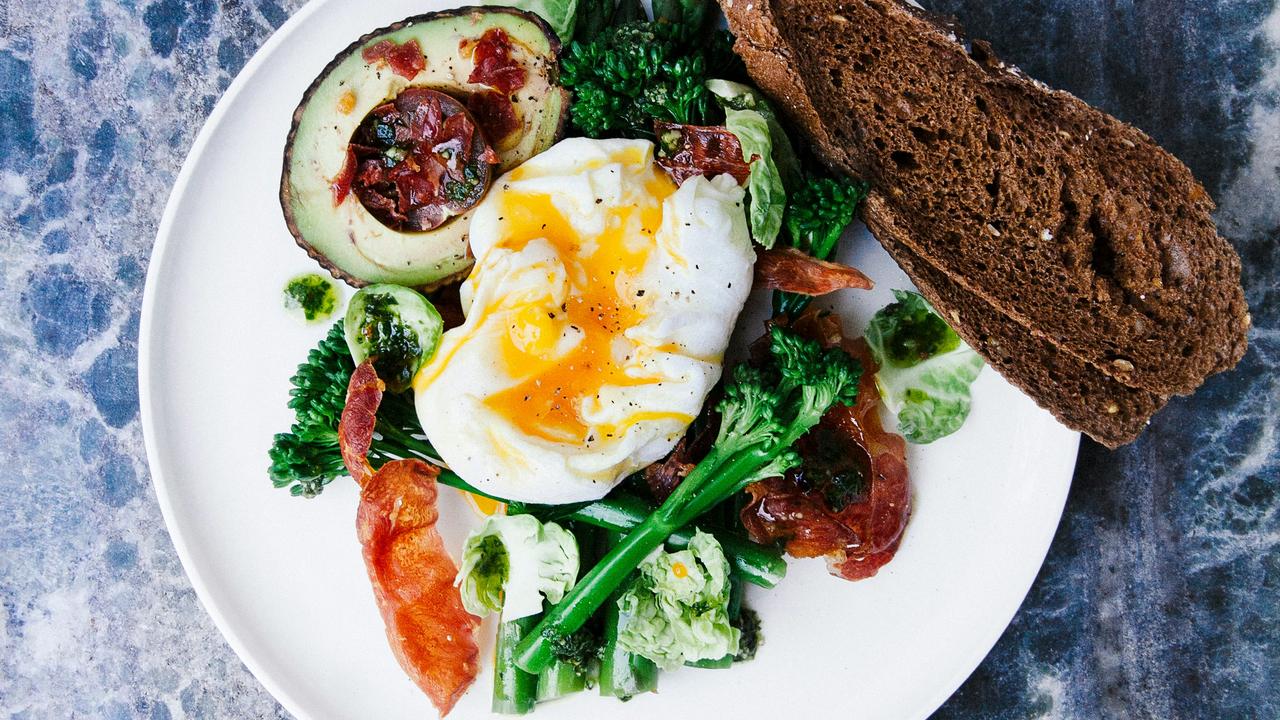 A plate of poached egg with avocado, greens, and bread.