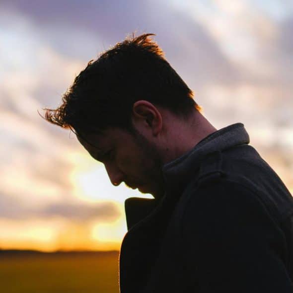 A man in silhouette looking down against a sunset sky.