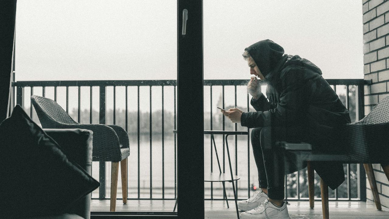 A hooded man smoking on a balcony.