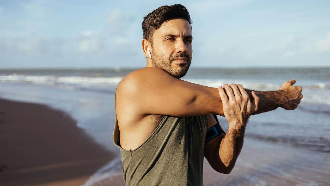 A man stretching his arm on a beach.