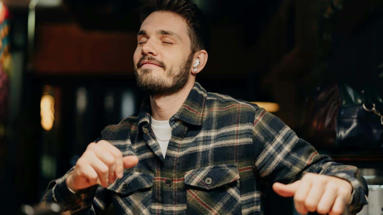 A man in a plaid shirt enjoying music with earbuds.