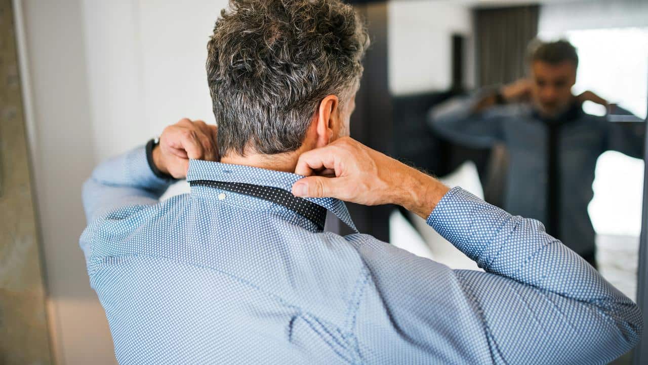 A man adjusting a tie in front of a mirror.