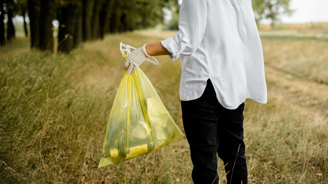 A person carrying a yellow trash bag in a field.