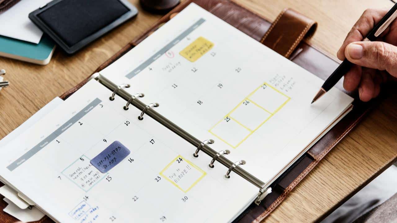 A person’s hand holding a pen over a planner.