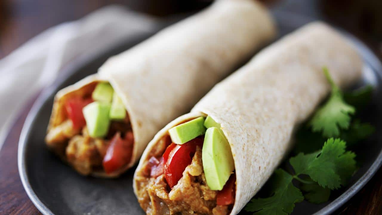 A pair of burritos with avocado.