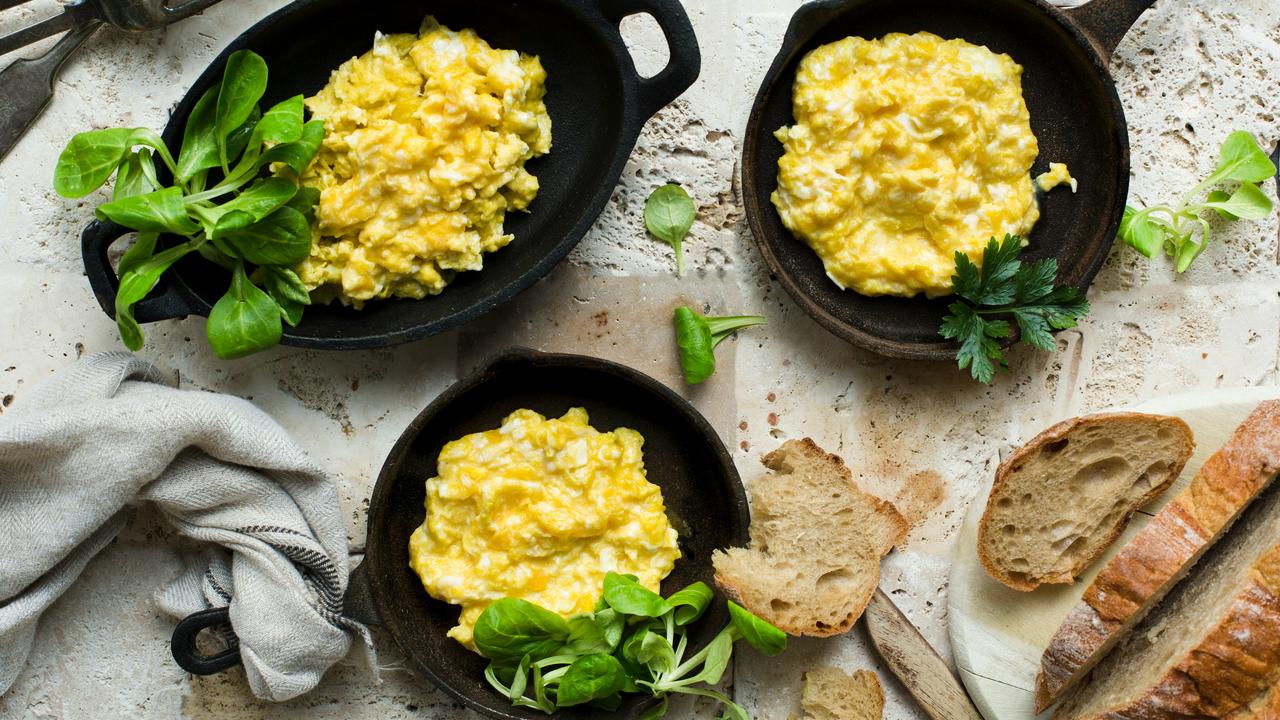 A trio of skillets with scrambled eggs and bread.