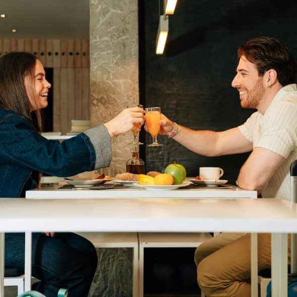A man and woman clinking glasses of orange juice at a café table.