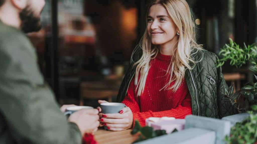 A woman smiling while having coffee with someone.