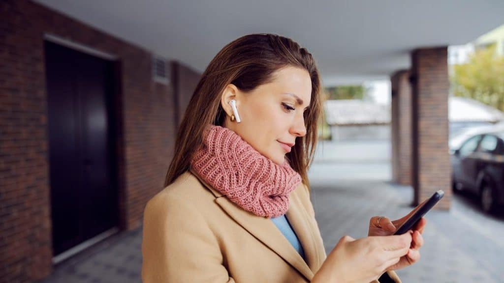 A woman wearing a coat and pink scarf using her phone.