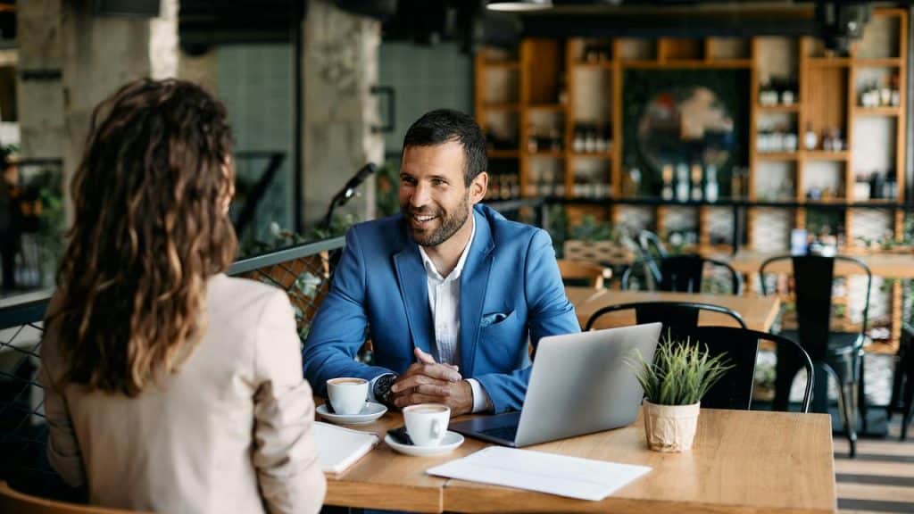 A man in a blue blazer talking with a woman at a café table.