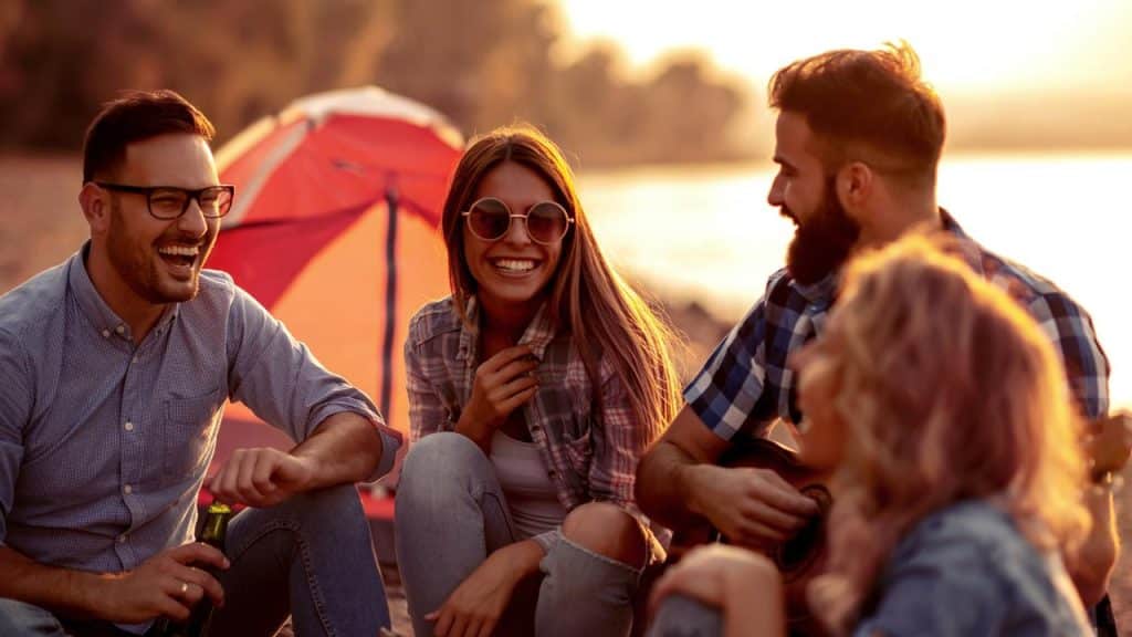 A group of friends laughing near a tent at sunset.