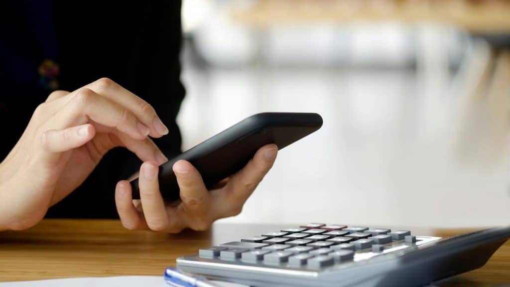 A person using a smartphone beside a calculator.