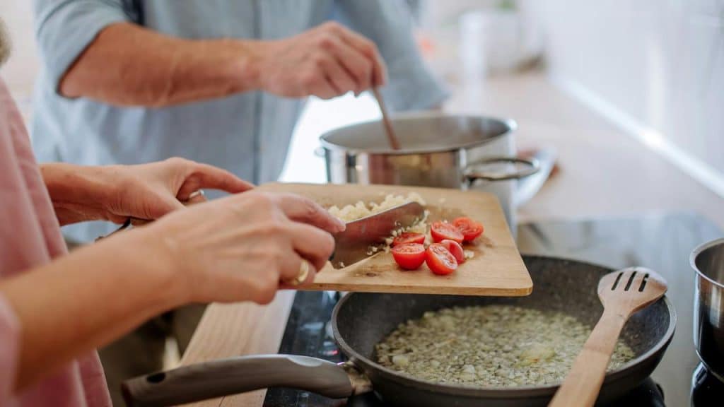 A person adding chopped vegetables to a frying pan.