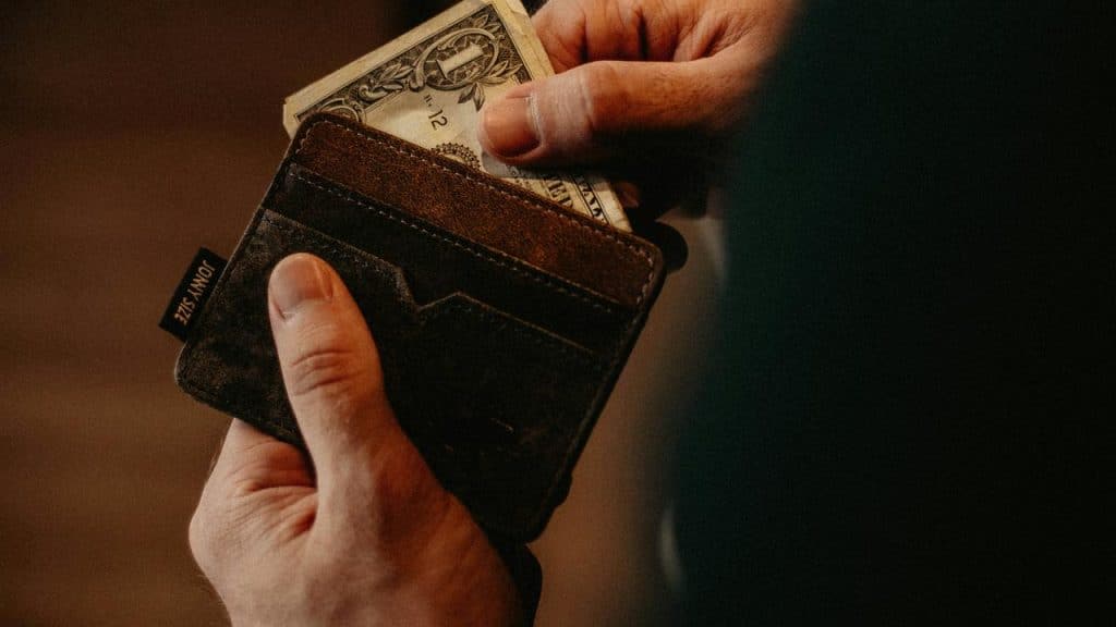 A person putting a dollar bill into a wallet.
