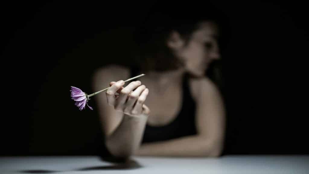 A sad woman holding one flower