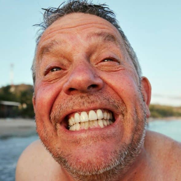 A smiling, happy middle-aged man with a beard is at the beach.