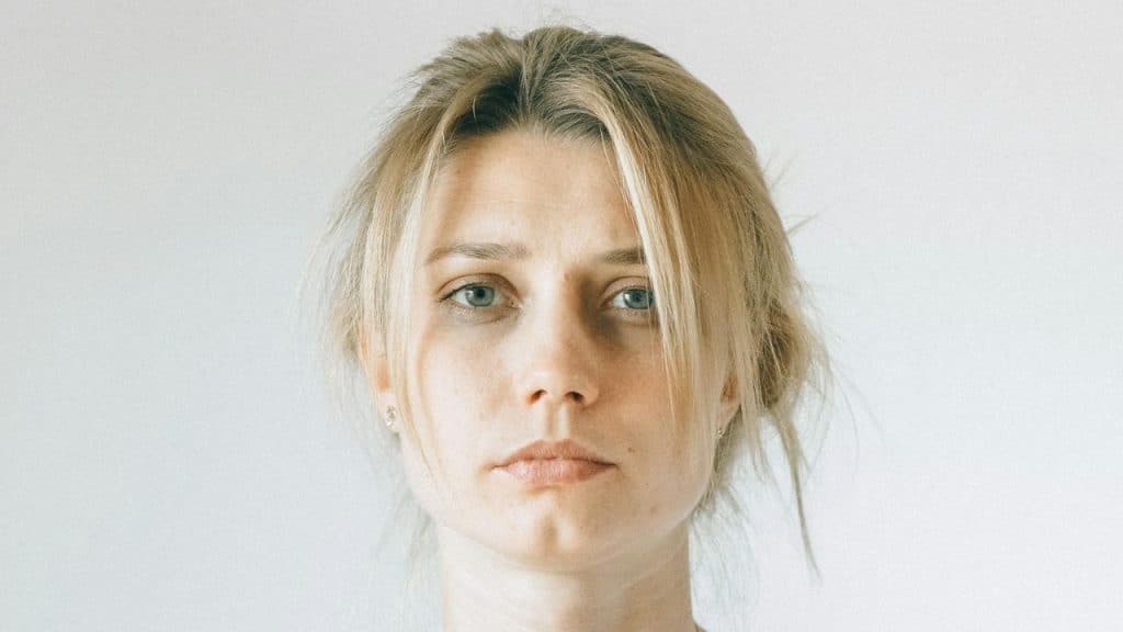 A portrait of a serious-looking young woman with blonde hair and blue eyes.