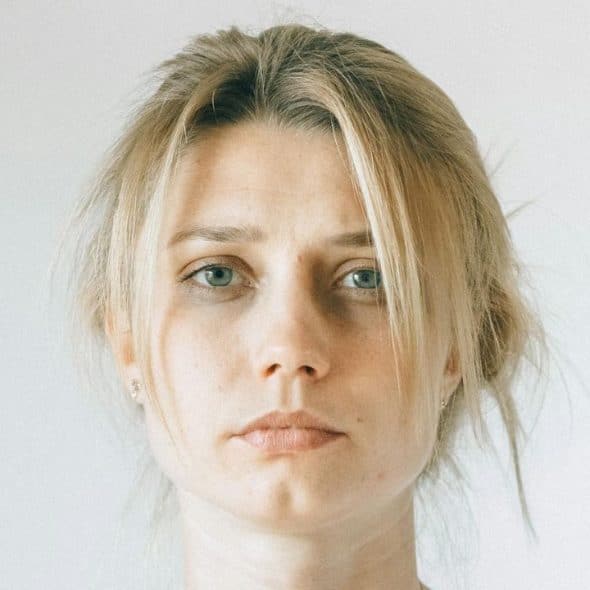 A portrait of a serious-looking young woman with blonde hair and blue eyes.