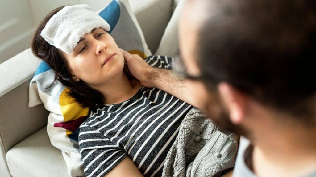 A concerned man comforting his sick wife, who has a towel on her forehead.