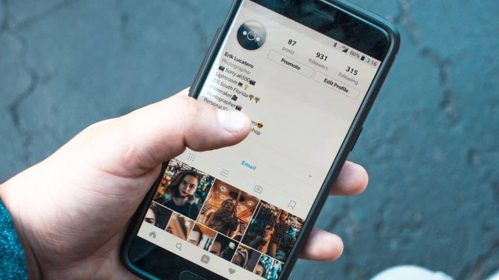 A hand holds a phone displaying a person's social media profile page.