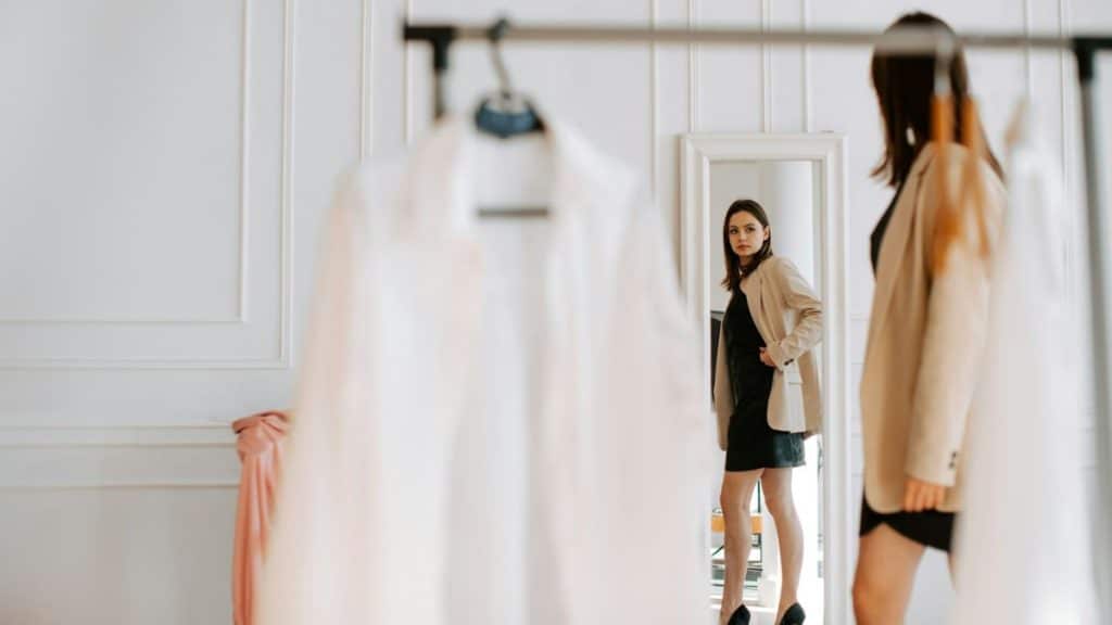 A woman poses and looks at herself in a mirror while trying on a new outfit.