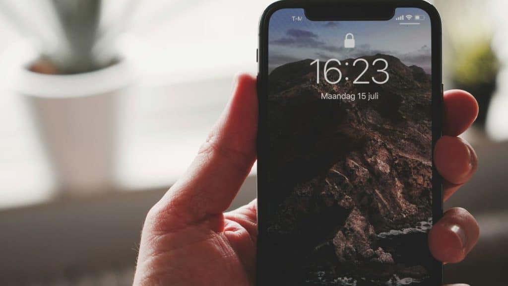 A hand holds an iPhone displaying a locked screen with a mountain wallpaper.
