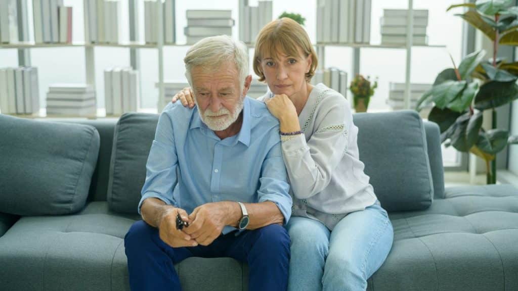 A concerned woman is comforting a sad-looking man on a couch.