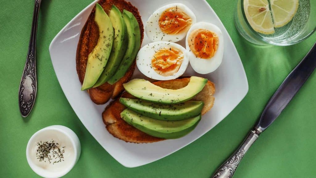 A plate of avocado toast with boiled eggs and seasoning.