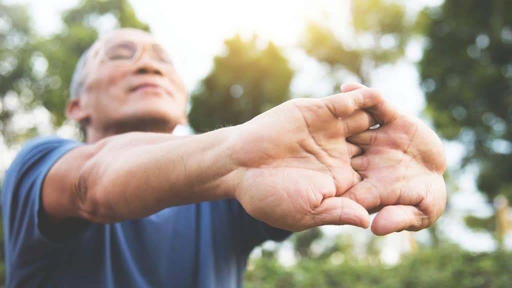 An older man stretching his arms outdoors.