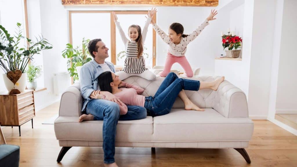 A family relaxing on the couch while two children play and laugh.