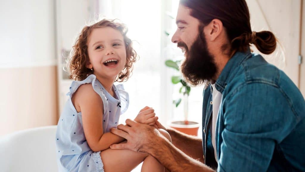 A father smiling and playing with his laughing young daughter.
