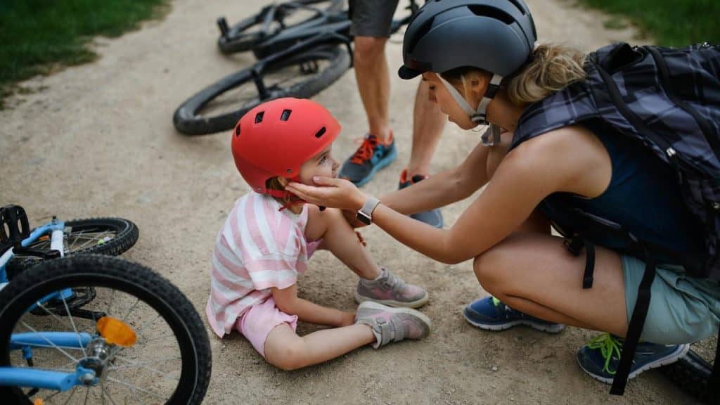 A woman checking on a young girl wearing a helmet after a bike ride.