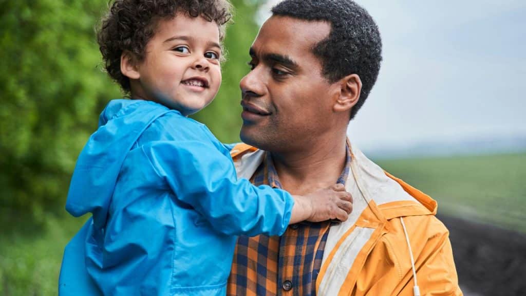 A father holding his smiling young son outdoors.