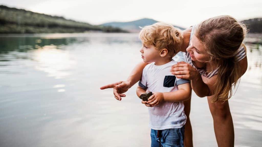 A mother pointing something out to her young son by a lake.