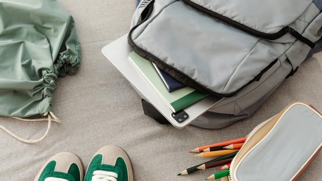 A child’s school supplies and backpack laid out on a bed.