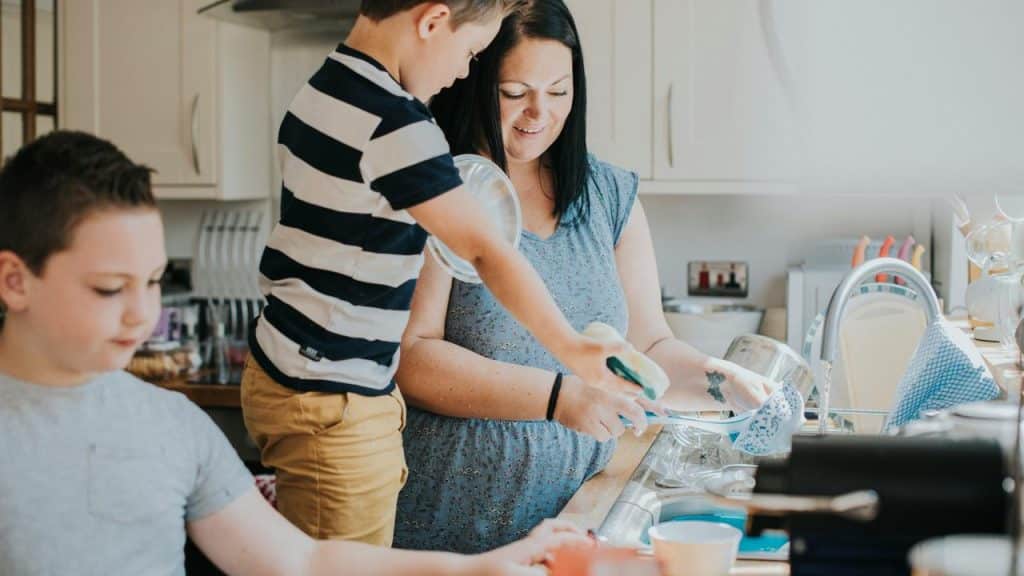A mother washing dishes with her two sons in the kitchen.