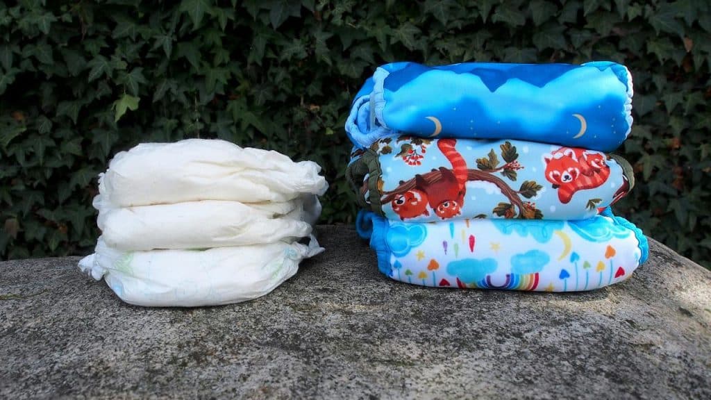 A stack of disposable diapers next to a stack of colorful cloth diapers.