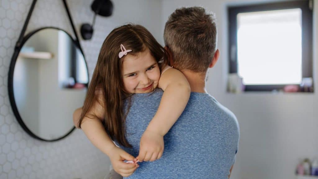 A man carrying his smiling daughter in his arms.